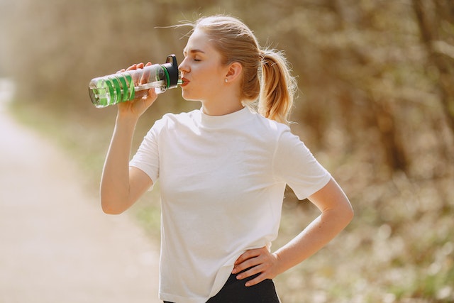 Lady drinking water to hydrate after an exercise.